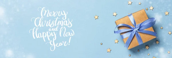 Cadeaudoosje met blauw lint op een blauwe achtergrond met decoratieve sterren. Vrolijk kerstbericht toegevoegd. Cadeauconcept voor een geliefde, vakantie. Banner .Flat lay, bovenaanzicht — Stockfoto