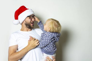 Gözlüklü genç bir adam ve Noel Baba şapkası beyaz arka planda bir çocukla oynuyor. Noel konsepti, aileyle kutlama, aile tatilleri.