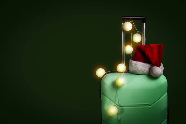 Plastový kufr, čepice Santa Claus a věnce na tmavě zelené ba — Stock fotografie