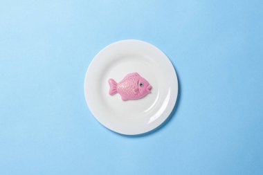 Mavi arka planda besin şeklinde plastik oyuncak balıklı beyaz tabak. Konsept yapay gıda, uygun beslenme, diyet, uygun gıdalar. Düz yatış, üst görünüm