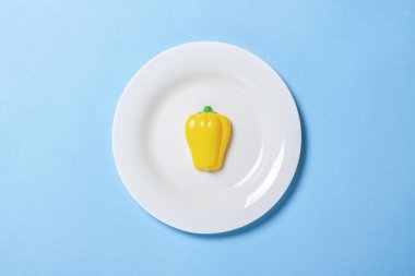 Kırmızı biberli beyaz tabak. Mavi arka planda kırmızı biber oyuncakları. Konsept yapay gıda, uygun beslenme, diyet, uygun gıdalar. Düz yatış, üst görünüm