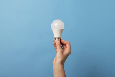 Kadın eli mavi arka planda Led lambasını tutuyor. Enerji tasarrufu kavramı, alternatif enerji kaynakları, fikir