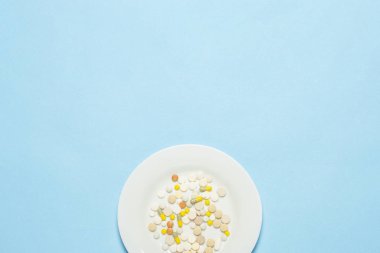 Mavi arka planda beyaz tabakta bir sürü hap var. Uykusuzluk, ilaç seçimi, vitamin, tarım ilaçları yüzünden kilo kaybı. Düz yatış, üst görünüm