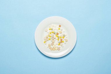 Mavi arka planda beyaz tabakta bir sürü hap var. Uykusuzluk, ilaç seçimi, vitamin, tarım ilaçları yüzünden kilo kaybı. Düz yatış, üst görünüm