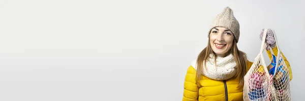 Eine junge Frau mit einem Lächeln hält eine Einkaufstasche mit Geschenken vor hellem Hintergrund. Konzept der Winterferien, Weihnachten, Neujahr, Verkauf, Geschenkeinkauf. Stimmung, Emotionen, Überraschung, Schock. Banner — Stockfoto