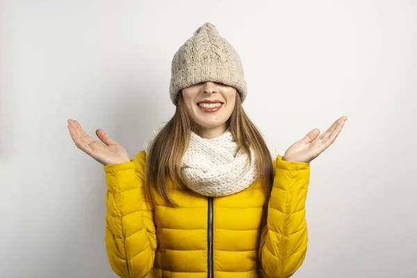 Jovem mulher colocar um chapéu sobre os olhos, um lenço e uma jaqueta amarela em um fundo claro. Conceito de inverno, moda de inverno, roupas de inverno — Fotografia de Stock