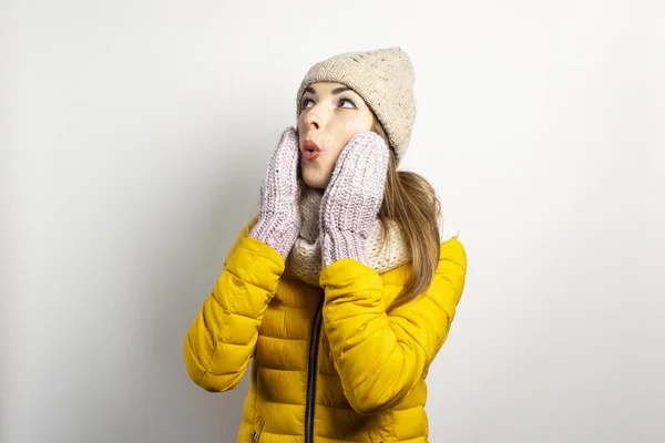 Νεαρή γυναίκα με καπέλο και γάντια σε ανοιχτόχρωμο φόντο. Χειμερινή ιδέα, χειμερινή μόδα, χειμωνιάτικα ρούχα. Αστεία διάθεση, συναισθήματα, έκπληξη, σοκ — Φωτογραφία Αρχείου