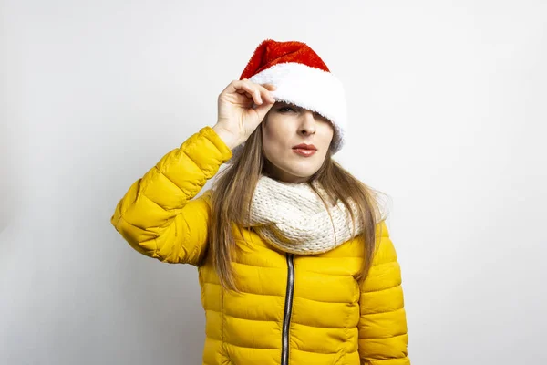 Mujer joven mira desde debajo de los sombreros de Santa Claus con los ojos puestos en un fondo claro. Concepto de invierno, vacaciones de invierno, Navidad, Año Nuevo. Humor divertido, emociones, sorpresa, shock — Foto de Stock
