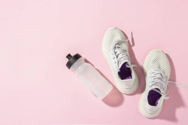 Pembe arka planda beyaz spor ayakkabılar ve güneş ışığı altında bir şişe su. Kavram, koşu, koşma, spor, çapraz uyum. Sabah koşusu. Pankart. Düz yatış, üst görünüm