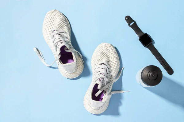 Fitness tracker, White sneakers and a bottle of water under morning sunlight on a blue background.Jogging, running, fitness, cross fit, hard workout. Morning run. Banner. Flat lay, top view