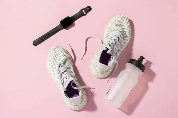 Fitness tracker, White sneakers and a water bottle under the morning sunlight on a pink background. Concept, jogging, running, fitness, cross fit. Morning run. Banner. Flat lay, top view