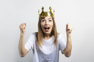 Kafasında taç olan genç bir kadın duygusal olarak seviniyor ve hafif bir arka planda kutluyor. Duygusal kahkaha, sürpriz, şok. Kraliçe kavramı, şans, zafer, hayal, amaç, arzu. Pankart