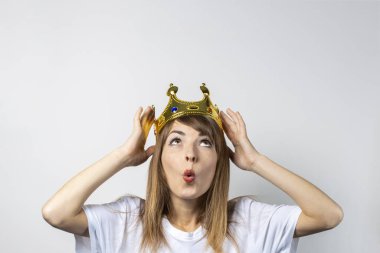 Kafasında taç olan genç bir kadın ve hafif bir arka planda şaşırmış bir yüz. Duygusal kahkaha, sürpriz, öpücük, şok. Kraliçe konsepti, şans, en iyisi, kazanmak, zafer. Pankart