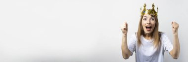Kafasında taç olan genç bir kadın duygusal olarak seviniyor ve hafif bir arka planda kutluyor. Duygusal kahkaha, sürpriz, şok. Kraliçe kavramı, şans, zafer, hayal, amaç, arzu. Pankart