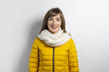 Genç bir kadın sarı bir ceket ve açık arkaplanda bir eşarpla jestler yapıyor. Duygular güler, şaşırtır, öper
