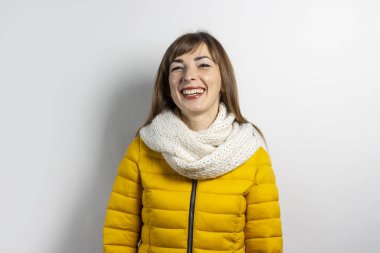 Genç bir kadın sarı bir ceket ve açık arkaplanda bir eşarpla jestler yapıyor. Duygular güler, şaşırtır, öper