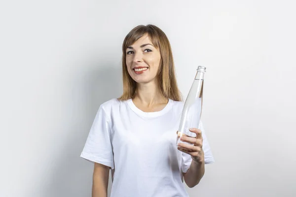 Une jeune femme tient une bouteille avec de l'eau claire sur un fond clair. Bannière. Le concept de soif, chaleur, santé et soins de beauté, équilibre hydrique — Photo