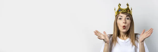 Young woman with a crown on her head and a surprised face on a light background. Emotion laughter, surprise, kiss, shock. The concept of a queen, luck, the best, win, victory. Banner — Stock Photo, Image