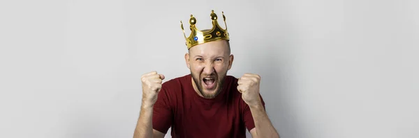 Un joven con una corona en la cabeza se regocija o celebra algo sobre un fondo claro. Concepto es rey, suerte, ganancia, rico, sueño, meta, aspiración. Banner — Foto de Stock