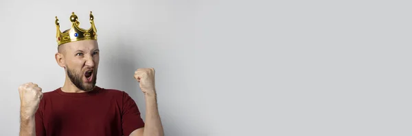 Un joven con una corona en la cabeza se regocija o celebra algo sobre un fondo claro. Concepto es rey, suerte, ganancia, rico, sueño, meta, aspiración. Banner — Foto de Stock