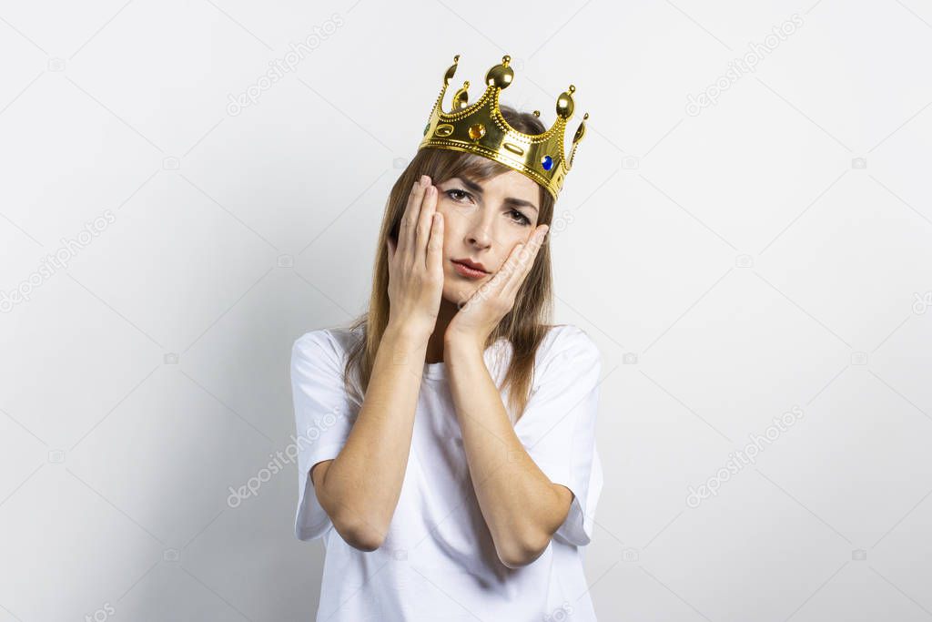 Young woman with a crown on her head and a sad face on a light background. Concept of a queen, luck, illness, boredom win, problems, dream, goal, aspiration. Banner