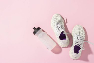 Pembe arka planda beyaz spor ayakkabılar ve güneş ışığı altında bir şişe su. Kavram, koşu, koşma, spor, çapraz uyum. Sabah koşusu. Pankart. Düz yatış, üst görünüm