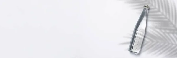 Botella de agua cristalina pura sobre fondo blanco bajo hojas de palma y luz solar. Banner. Concepto de sed, calor, verano, trópico. Piso tendido, vista superior —  Fotos de Stock