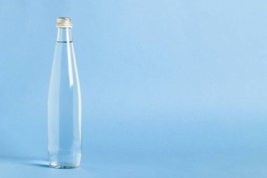 Mavi zemin üzerinde berrak, ferahlatıcı su bulunan cam şişe. Güzellik ve sağlık kavramı, su dengesi, susuzluk, yaz