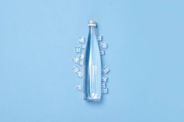 Buz küpleriyle mavi arka planda berrak su bulunan cam şişe. Sağlık ve güzellik kavramı, su dengesi, susuzluk, sıcaklık, yaz. Düz yerde, üst tarafta. Pankart