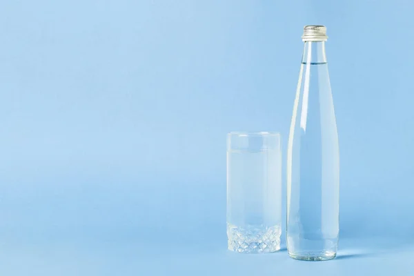 Glass bottle and glass with crystal clear refreshing water on a blue background. Concept of beauty and health, water balance, thirst, summer