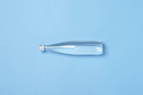 Скляна пляшка з чистою водою на синьому фоні. Концепція здоров'я та краси, баланс води, спрага, спека, літо. Плоский прошарок, вид зверху — стокове фото