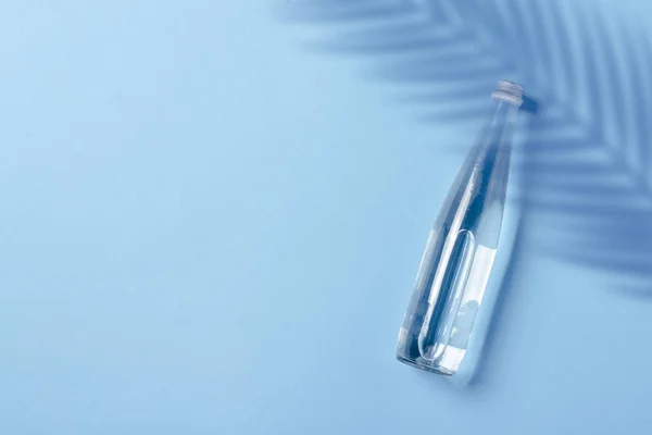 Скляна пляшка з чистою водою на синьому фоні. Концепція здоров'я та краси, баланс води, спрага, спека, літо. Плоский прошарок, вид зверху — стокове фото