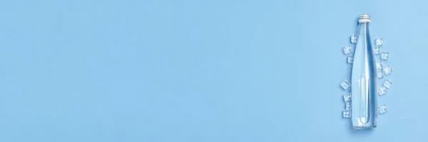 Glazen fles met helder water op een blauwe achtergrond met ijsblokjes. Concept van gezondheid en schoonheid, waterbalans, dorst, hitte, zomer. Vlakke lay, bovenaanzicht. Banner — Stockfoto