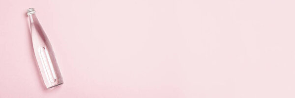 Стеклянная бутылка с чистой водой на розовом фоне. Концепция здравоохранения, водного баланса, красоты и здоровья. Баннер. Плоский, вид сверху