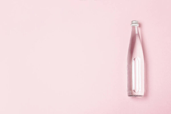 Стеклянная бутылка с чистой водой на розовом фоне. Концепция здравоохранения, водного баланса, красоты и здоровья. Баннер. Плоский, вид сверху