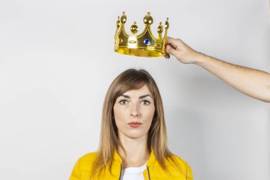 Sarı ceketli genç bir kadın ve hafif arka planda bir el kafasının üstünde bir taç tutuyor. Kavram kraliçesi, hırs, hayal, arzu, ego