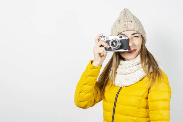 Mujer joven con una chaqueta amarilla y sombrero sostiene una cámara en sus manos y toma una foto sobre un fondo claro. Concepto de belleza y moda, invierno, otoño, tecnología. Banner — Foto de Stock
