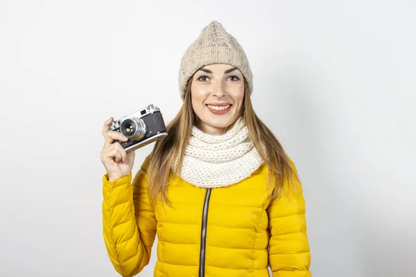 Jovem com sorriso em uma jaqueta amarela e chapéu segura uma câmera em suas mãos em um fundo leve. Conceito de beleza e moda, inverno, outono, tecnologia. Banner — Fotografia de Stock