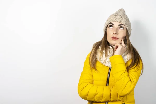 Mulher nova em uma jaqueta abaixo amarela e chapéu com uma cara pensativa em um contexto leve. Conceito sonho, pensamento, escolha, decisão, planejamento. Banner — Fotografia de Stock