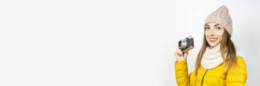 Sarı ceketli ve şapkalı gülümseyen genç bir kadın hafif arka planda elinde bir kamera tutuyor. Güzellik ve moda kavramı, kış, sonbahar, teknoloji. Pankart
