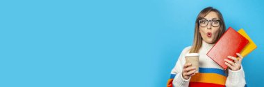 Şaşırmış bir yüzü olan genç bir kadın mavi arka planda kitap ve bir bardak kahve ya da çay tutuyor. Eğitim kavramı, üniversite, seans, sınav, kariyer seçimi. Pankart