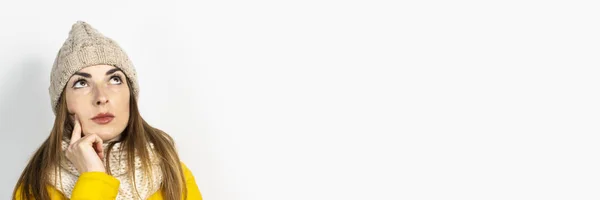 Mujer joven con una chaqueta amarilla y un sombrero con una cara pensativa sobre un fondo claro. Concepto sueño, pensamiento, elección, decisión, planificación. Banner — Foto de Stock