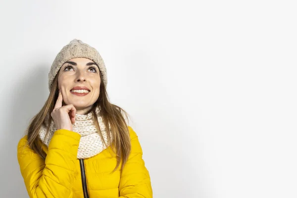 Mujer joven con una chaqueta amarilla y un sombrero con una cara pensativa sobre un fondo claro. Concepto sueño, pensamiento, elección, decisión, planificación. Banner — Foto de Stock