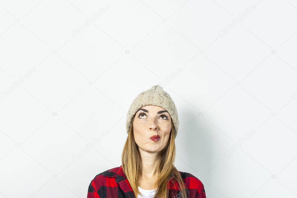 Young woman with a pensive face dreams of something in a hat, a red shirt and a white T-shirt on a white background. Stylish concept, dream, plan, goal, teenager style, shock, surprise. Banner