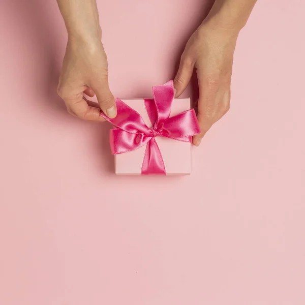 Les mains féminines tiennent, prennent, reçoivent un cadeau sur un fond rose. Concept de mariage, Saint Valentin, un cadeau pour un être cher. Couché plat, vue du dessus — Photo
