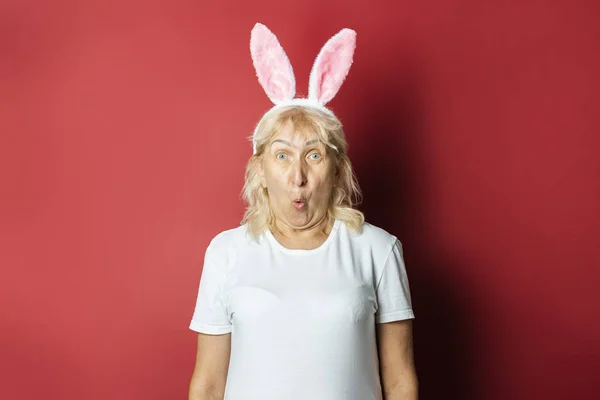 Anciana con orejas de conejo o liebre sobre un fondo rosa oscuro. Concepto de Pascua. Abuela. —  Fotos de Stock