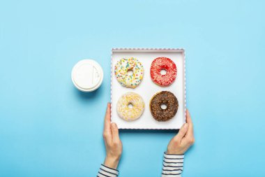 Kadın eli, donutlu bir kutu, mavi arka planda bir fincan kahve tutuyor. Şekerleme dükkanı, hamur işleri, kahve dükkanı. Pankart. Düz yatış, üst görünüm