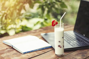 Laptop, açık günlüğü ve ferahlatıcı bir süt ile bir bardak çilek ahşap bir masa ve bahçenin arka planda ile iç. Doğada, freelancing, tatilde iş iş kavramı