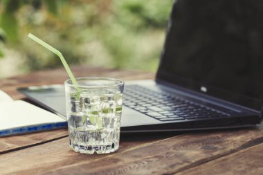Laptop, açık günlüğü ve bir bardak buz küpleri ve nane ile ferahlatıcı bir içki ile ahşap bir masaya bırakır. Doğada, freelancing, tatilde iş iş kavramı