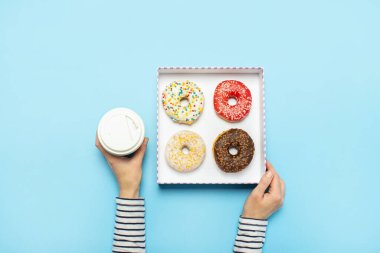 Kadın eli, donutlu bir kutu, mavi arka planda bir fincan kahve tutuyor. Şekerleme dükkanı, hamur işleri, kahve dükkanı. Pankart. Düz yatış, üst görünüm